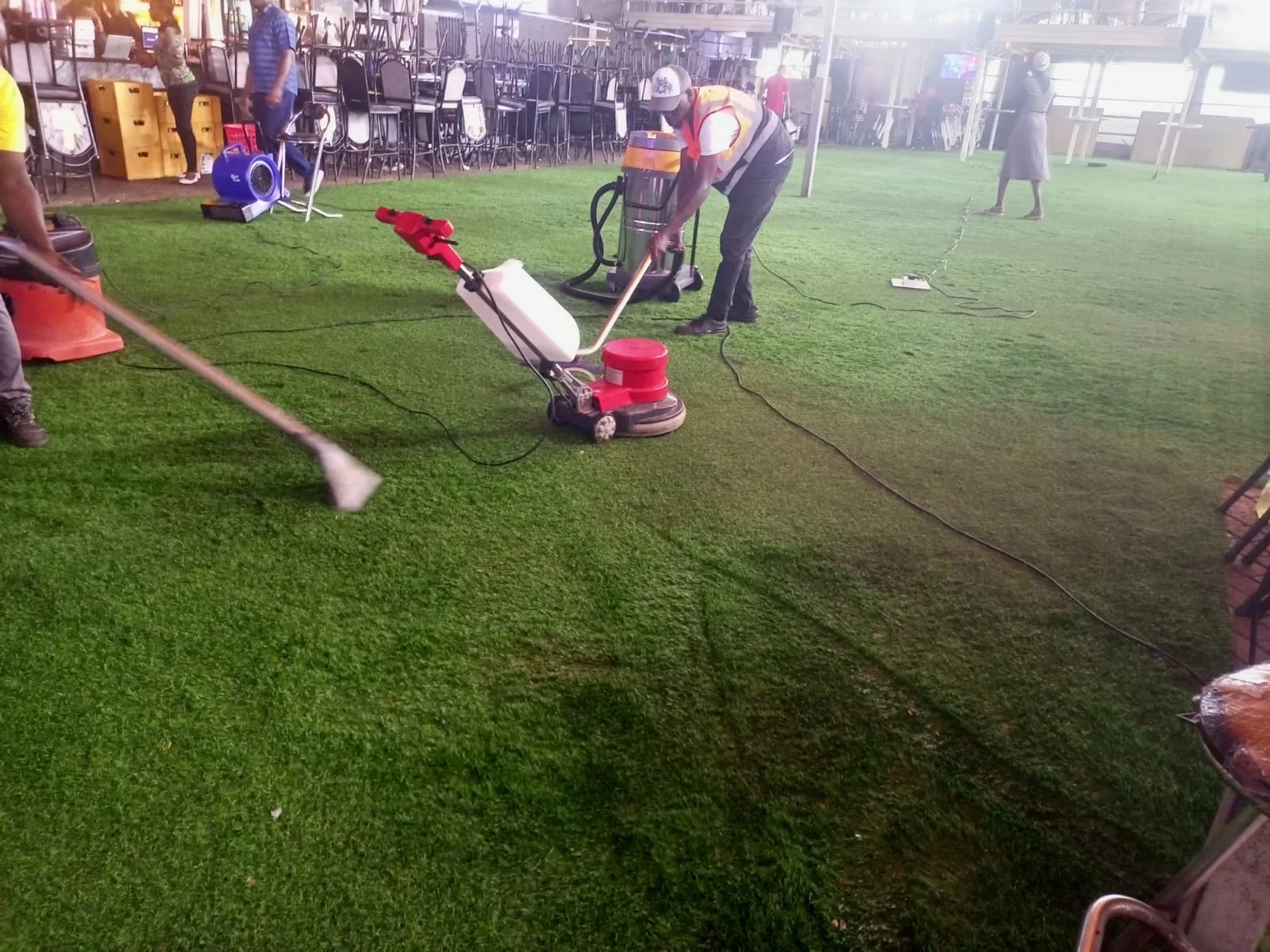 Cleaning team using floor-cleaning equipment on artificial turf at a venue